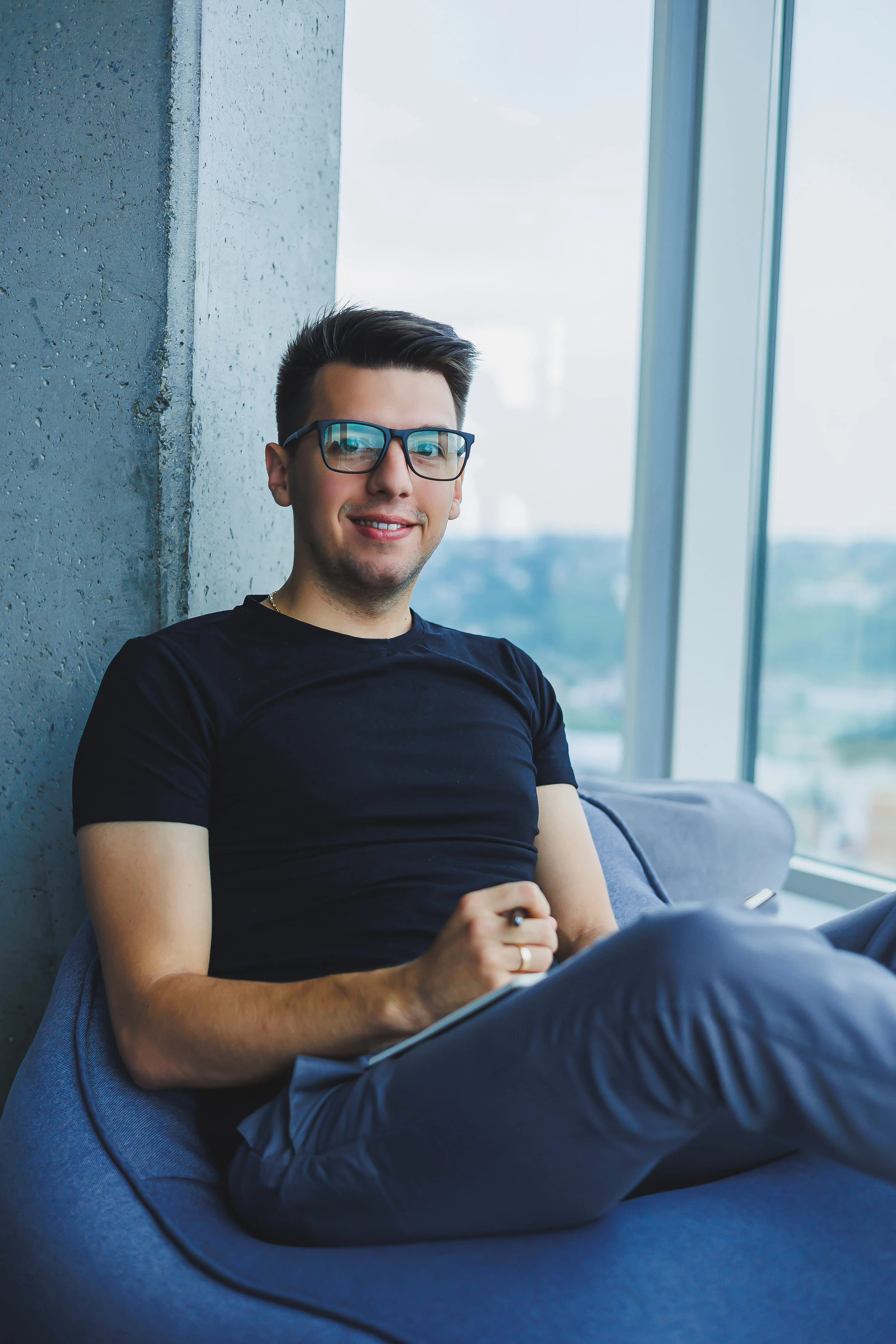 Man in glasses sits in blue chair with tablet