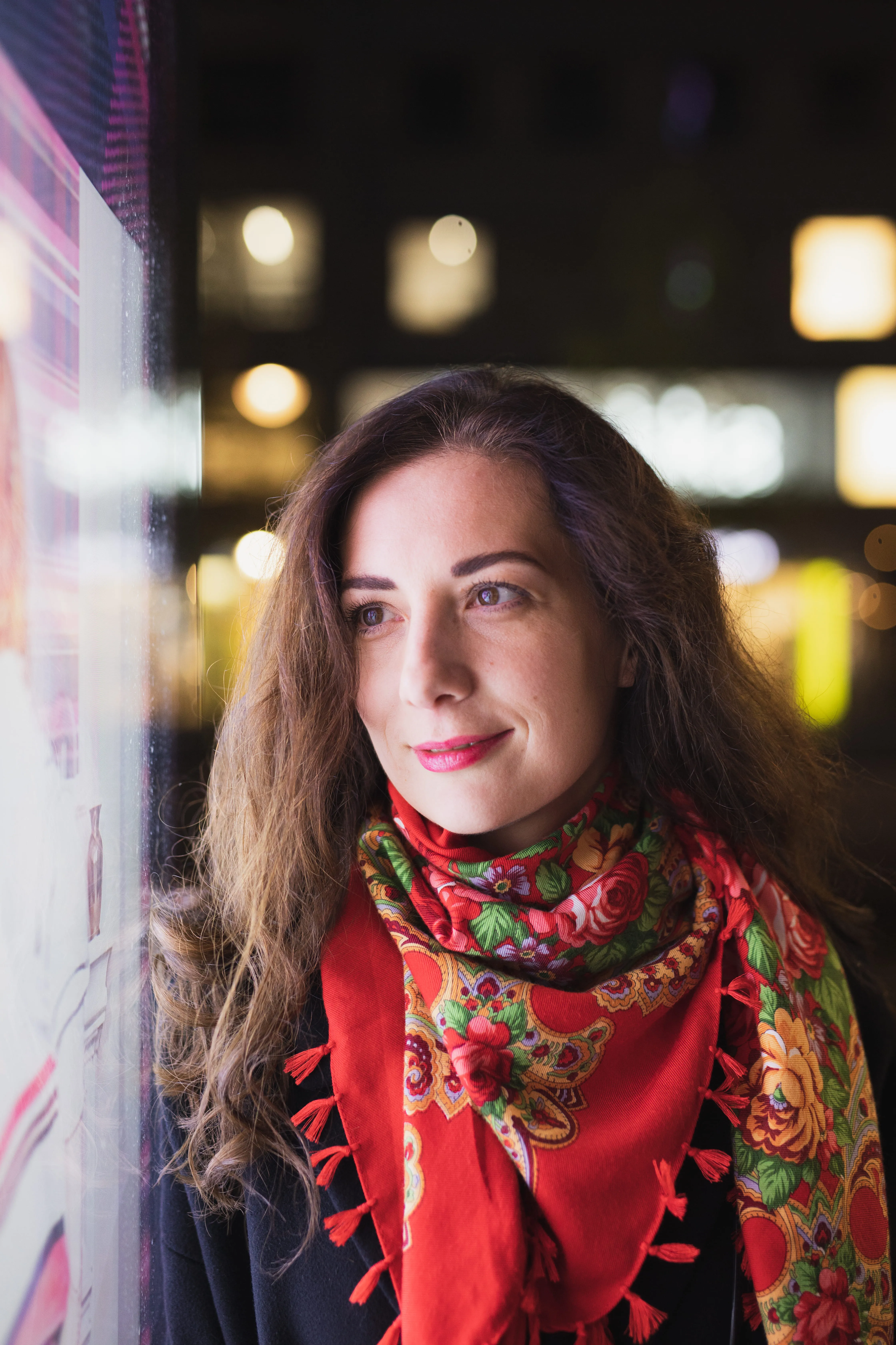 Woman with floral scarf looks out window at night